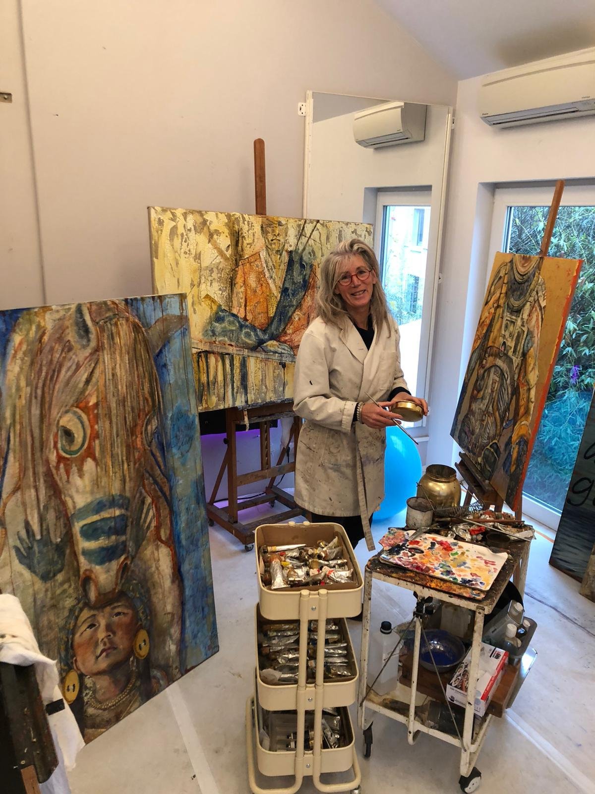 Isabelle Hugo dans son atelier, palette à la main, entourée de ses toiles